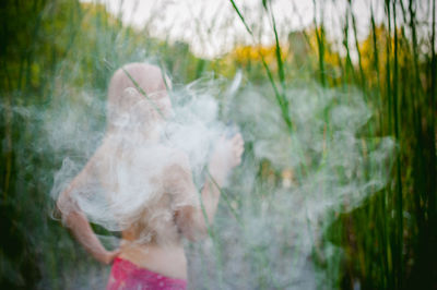 Rear view of shirtless young woman smoking while standing on grassy field