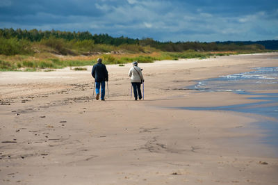 Rear view of old man and woman walking on beach against sky