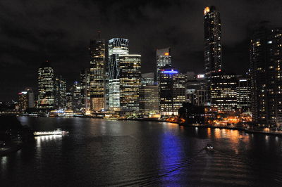 Illuminated buildings by river against sky at night