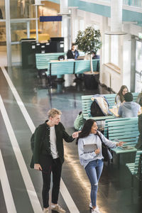 Male and female students pointing while walking in cafeteria at university