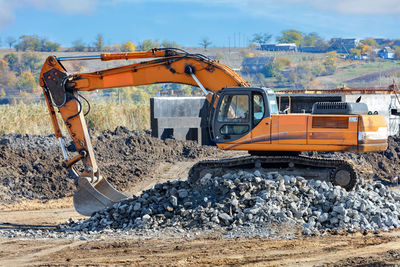 A construction crawler excavator climbs a pile of cobblestones during the construction of a road.