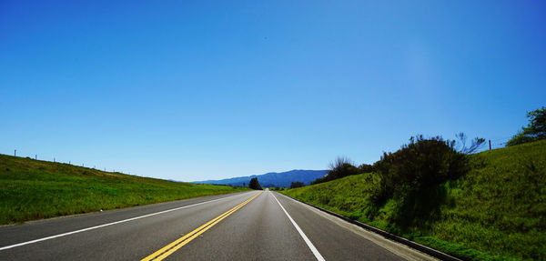 Road amidst green landscape against clear blue sky