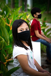 Two asian children wearing mask sitting in distance of 1 meter from others keeping distancing. 