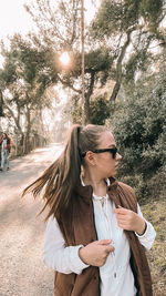 Side view of young woman standing against trees