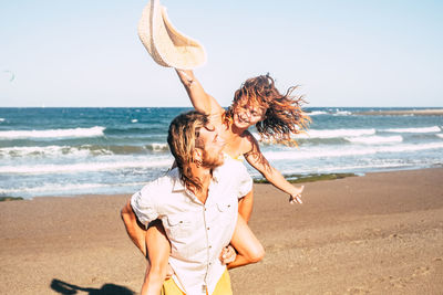 Smiling man carrying girlfriend on back at beach