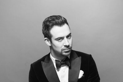 Close-up portrait of young man in suit standing against gray background