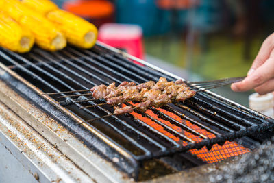 Cropped hand roasting meat on barbecue grill