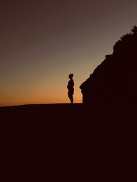 Silhouette man standing on shore against sky during sunset
