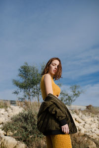 Young woman standing by tree against sky