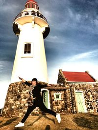 Portrait of young woman standing by lighthouse against sky