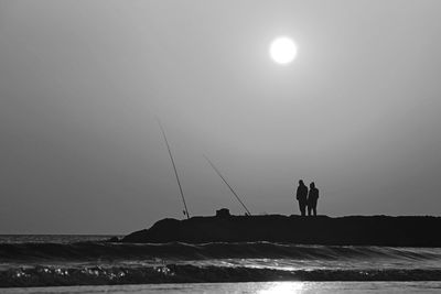 Silhouette people fishing in sea against clear sky