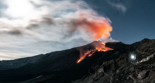 Panoramic image of volcano etna eruption at night with full moon. man with a torch lighting up 