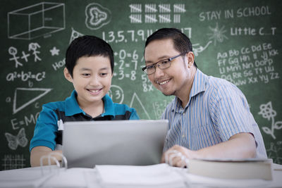 Boy with teacher at table against blackboard