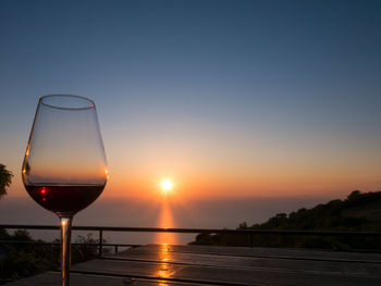 Close-up of wineglass against sky during sunset