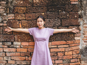 Portrait of a smiling young woman standing against brick wall