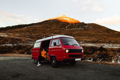 Young tourist in eyeglasses sitting in vintage automobile between deserted ground in snow near mountains