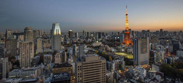 Illuminated tokyo tower in city against clear sky during sunset