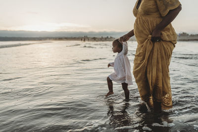 Young daughter and pregnant mother walking into the ocean