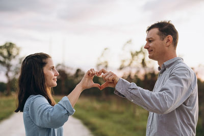 Side view of young couple making heart shape by hand