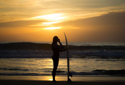 Silhouette of woman standing on beach at sunset