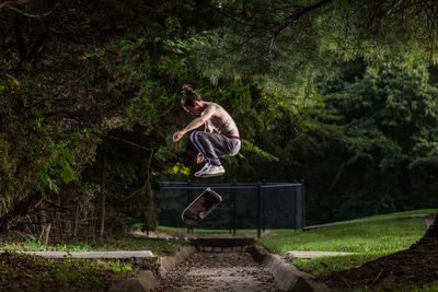 Full length of man doing stunt with skateboard at park 