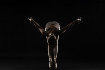 Ballet dancer stretching exercising against black background