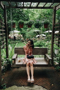 Full length of woman sitting on seat against trees