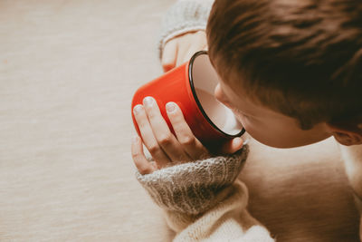 Hands in a sweater hold hot cocoa, in a red mug, top view. a cozy photo with a mug iwith copy space