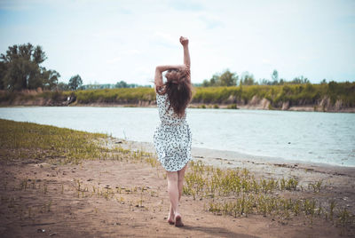 Full length of woman walking with arms raised by lake against sky