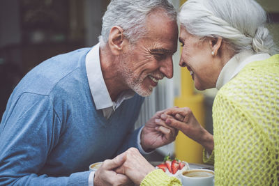 Smiling senior couple holding hands sitting at cafe