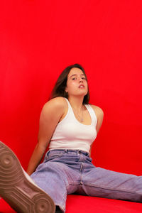 Portrait of young woman sitting against red background