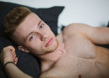 Close-up portrait of shirtless man lying on bed