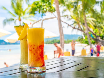 Yellow drink in glasses on table against swimming pool