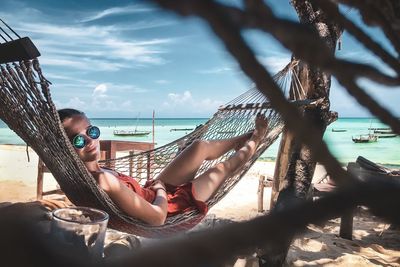 Portrait of woman relaxing on hammock at beach against sky