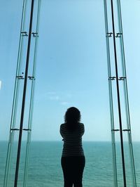 Rear view of woman standing by sea against clear sky