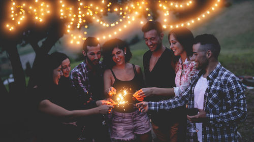 Happy friends burning sparklers in party at dusk