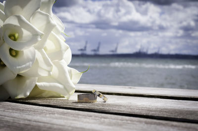 Close-up of wedding rings by flowers on pier