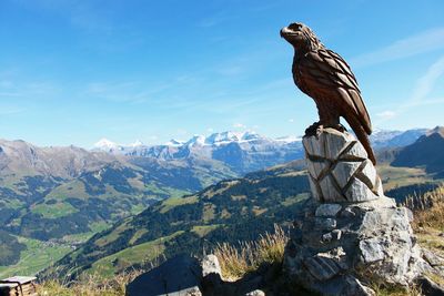 Bird perching on statue by mountain against sky