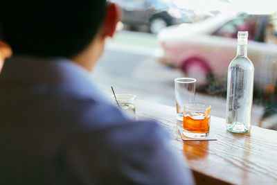 Rear view of man with drink on table against window in restaurant