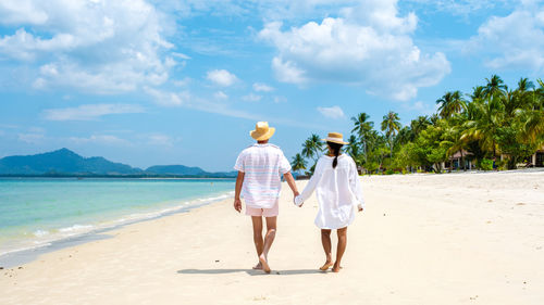 Rear view of couple walking at beach against sky