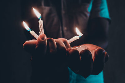 Midsection of man holding burning candles