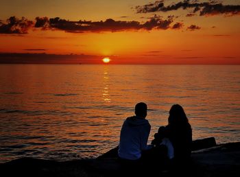 People looking at sea against sky during sunset