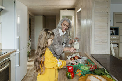 Grandmother and granddaughter unpacking fresh groceries in kitchen