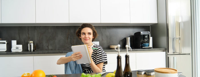 Portrait of young woman using mobile phone while sitting in kitchen