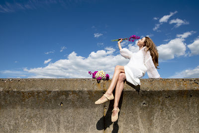 A girl sitting on the wall with field flowers in her hand