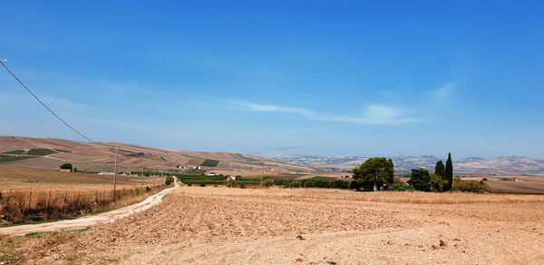 Dirt road amidst field against blue sky
