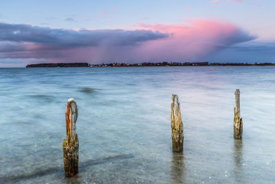 Wooden posts on beach against sky during sunset