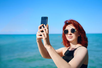 Portrait of young woman using mobile phone against sea