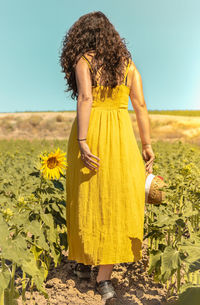 Full length of woman standing on sunflower field against clear sky