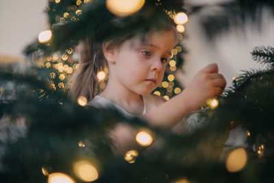 Toddler girl decorating christmas tree at home